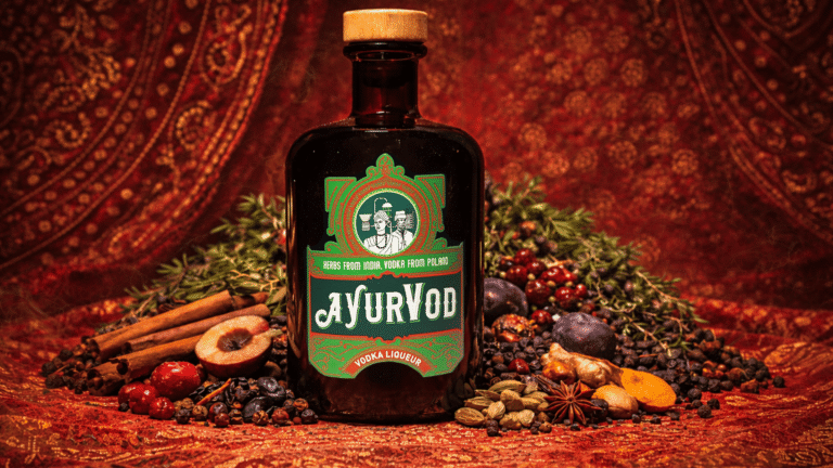 Butelka likieru ziołowego Ajurvod na tle nasion, owoców i orientalistycznych dywanów